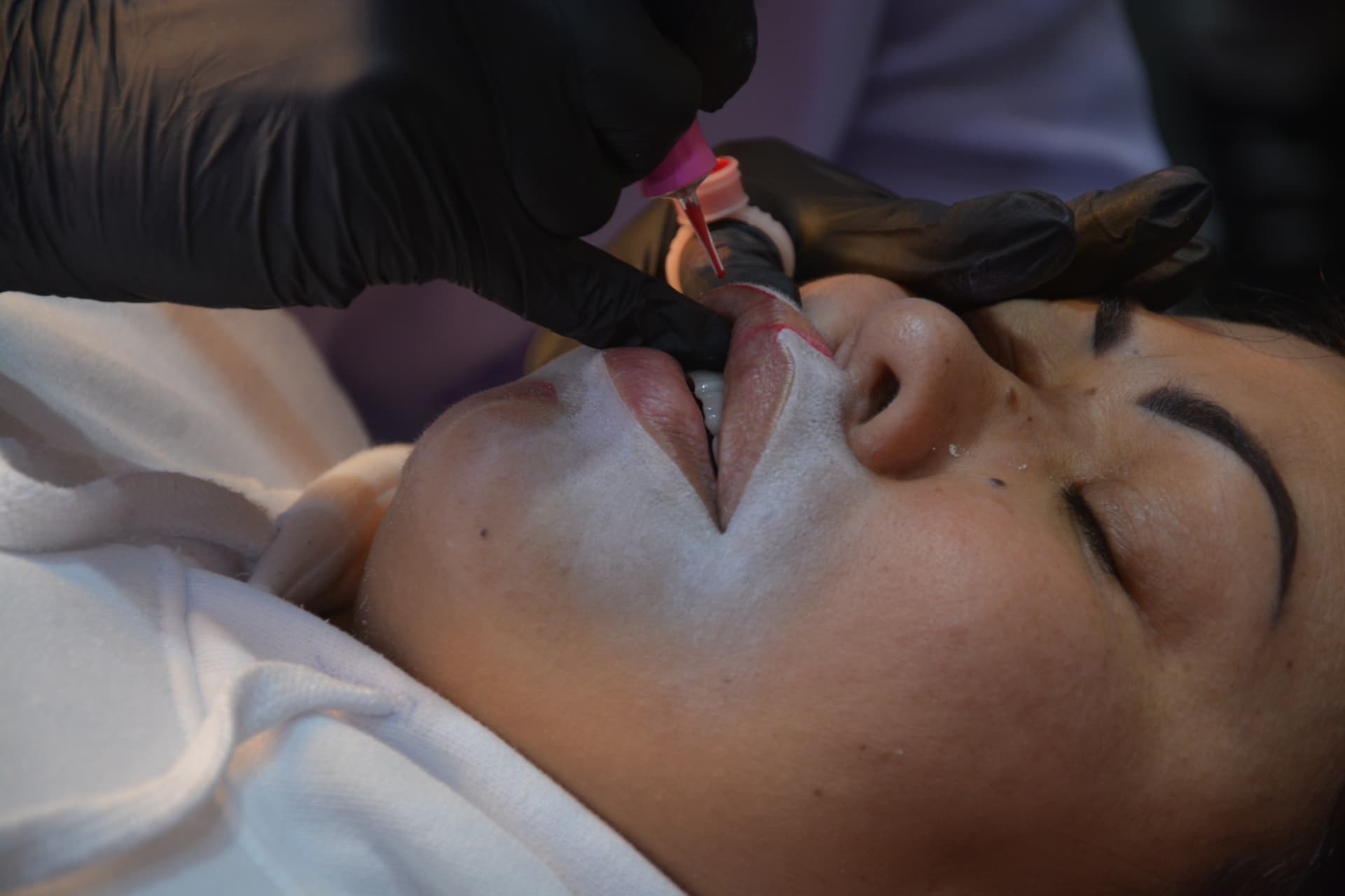 Procedimento de micropigmentação labial em andamento, com agulha aplicando pigmento no lábio